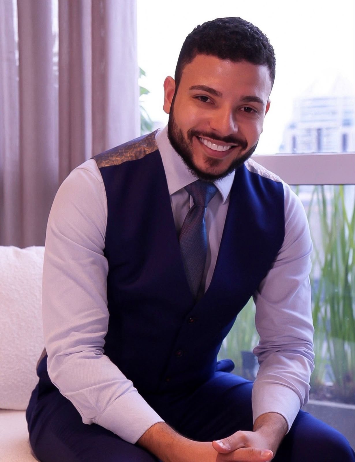 Dr. Mateus Bonutty sorrindo, de colete e gravata, sentado no consultório